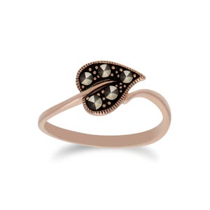 May include: A rose gold ring featuring a leaf design. The leaf is adorned with small, dark gray stones, creating a textured pattern. The ring's band curves gracefully, adding to its elegant appearance.