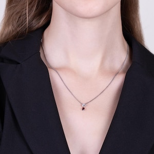 May include: A silver chain necklace with a small red gemstone pendant.