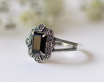 May include: A silver ring with a black gemstone set in a detailed, ornate design. The ring has a delicate, split band.