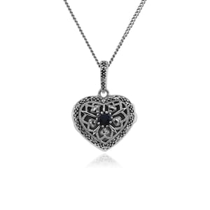 May include: A silver heart-shaped locket necklace with a black gemstone in the centre and a delicate filigree design. The locket is adorned with marcasite stones.