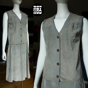May include: A gray suede vest and skirt set with a V-neck and button closure. The vest has a knit trim around the neckline and the skirt has a cable knit design.