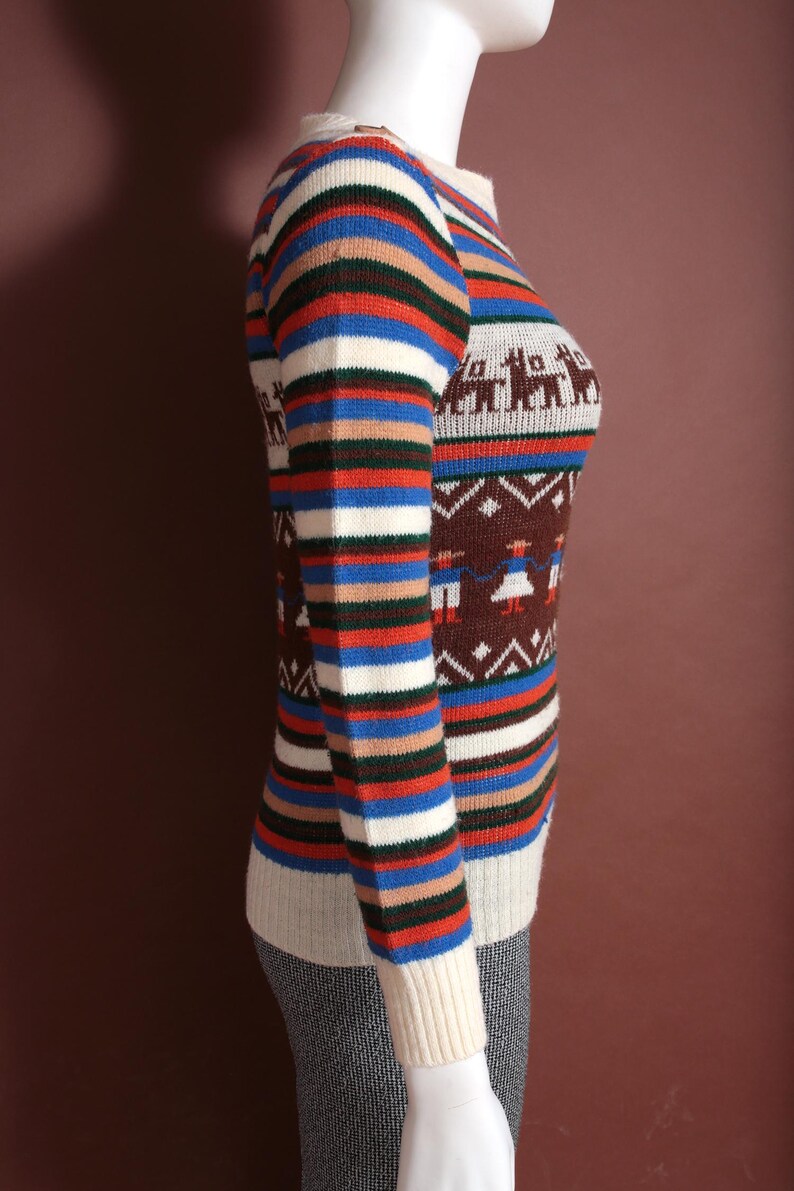 May include: A vintage-style sweater with a round neckline and long sleeves. The sweater features a striped pattern in blue, red, white, and brown. The lower portion has a brown background with white figures. The sleeves have a striped pattern.