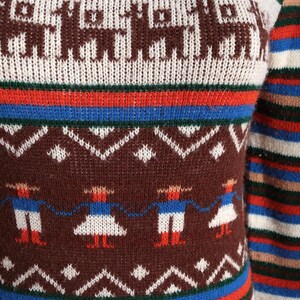 May include: A colorful sweater with a pattern of brown llamas and figures in traditional clothing. The sweater features horizontal stripes in red, blue, white, and brown. The sleeve is visible on the right side.