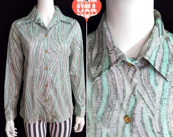May include: A long-sleeved shirt with a green and white abstract pattern. The shirt has a button-down collar and a button-up front.