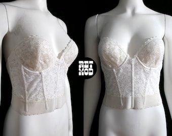 Puede incluir: Corsé blanco sin tirantes de encaje con varillas y cierre de gancho y ojo. El corsé está hecho de un delicado tejido de encaje blanco con un patrón floral.