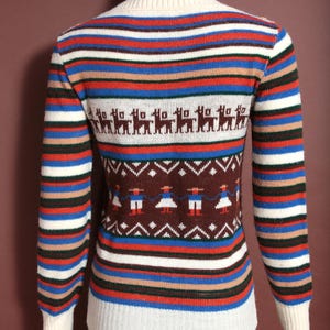 May include: A vintage sweater with horizontal stripes in red, blue, white, and brown. The sweater features a cream-colored neckline and cuffs. The design includes a pattern of llamas and figures in traditional clothing.