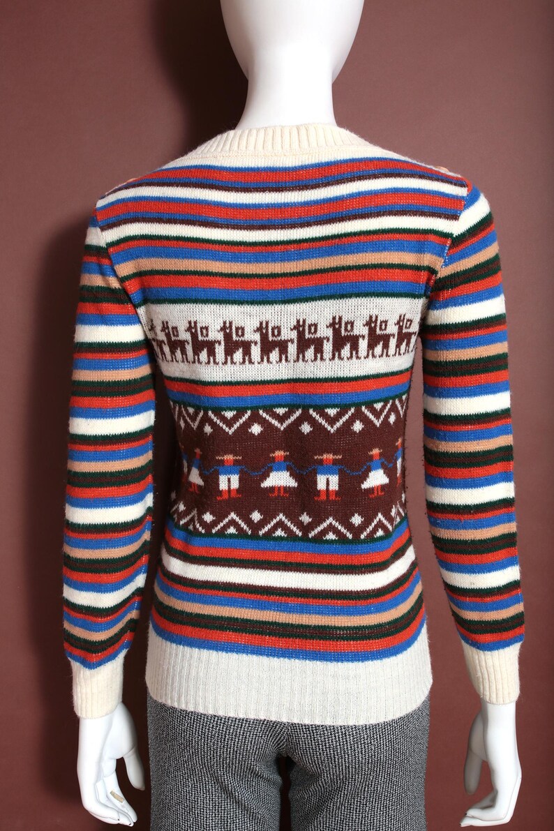 May include: A vintage sweater with horizontal stripes in red, blue, white, and brown. The sweater features a cream-colored neckline and cuffs. The design includes a pattern of llamas and figures in traditional clothing.