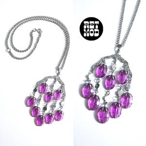 May include: A silver-toned necklace with a cascading pendant featuring faceted purple beads and small silver discs. The pendant is attached to a delicate chain. The image includes the text "RET MOD" in a black circle.