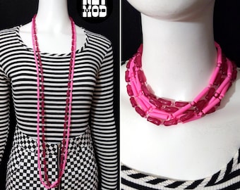 Peut inclure: Un long collier de perles en plastique rose et fuchsia. Le collier est superposé et a un look rétro et épais.