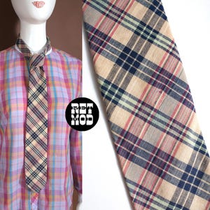Könnte beinhalten: Gezeigt wird eine karierte Krawatte in Beige, Marineblau, Rot und Grün. Die Krawatte ist geknotet und wird mit einem langärmeligen Button-Down-Hemd in einem rosa, lila und gelben Karomuster getragen. Das Bild enthält ein Logo in einem schwarzen Kreis.