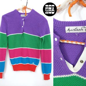 May include: A purple, green, pink, blue, and red striped sweater with a white button placket. The sweater has the text "Sonia Rykiel" on the label.