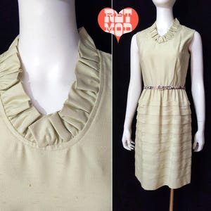 May include: A light green sleeveless dress with a ruffled neckline and a tiered skirt. The dress has a belt with a floral print.