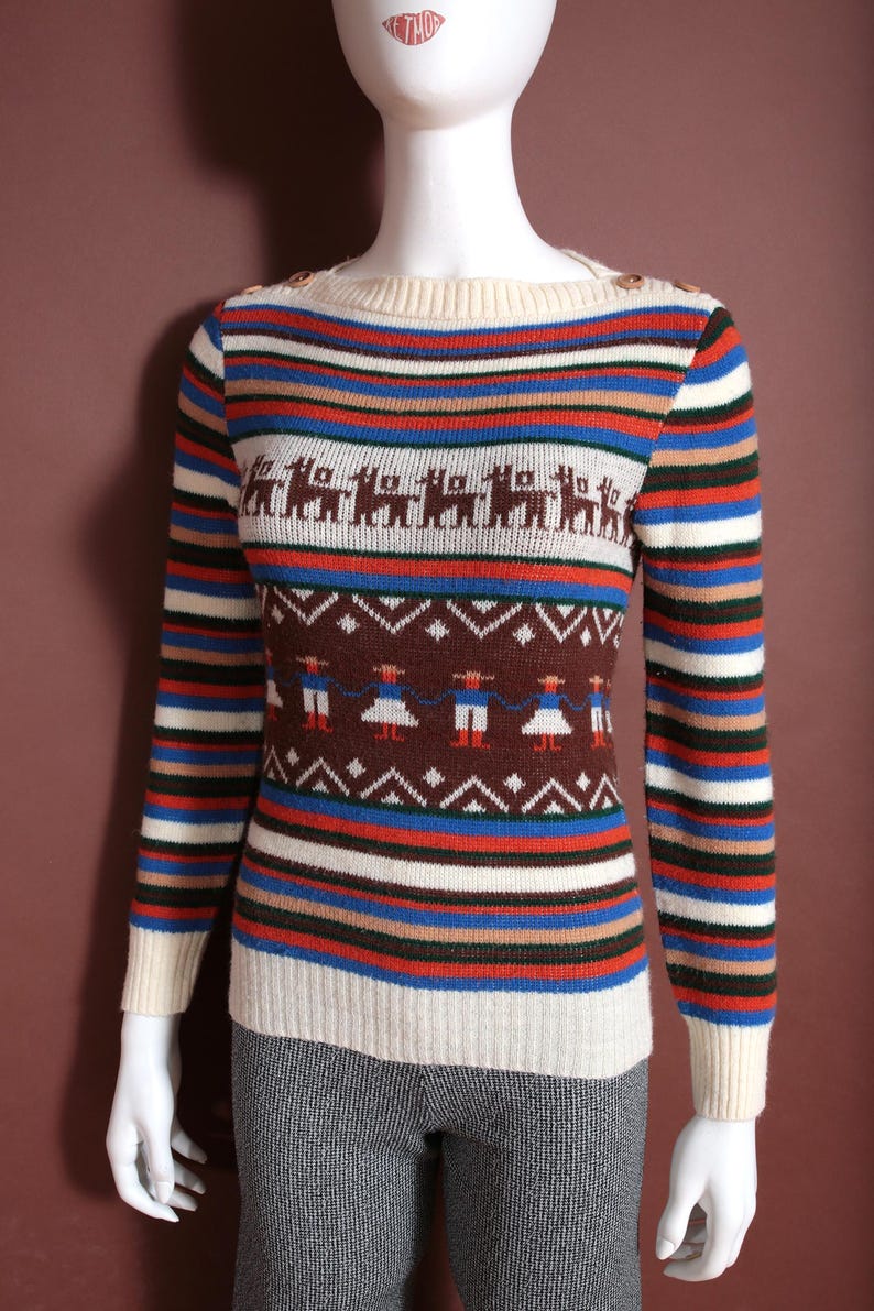 May include: A vintage-style sweater with a striped pattern in cream, blue, red, and brown. The sweater features a crew neck and long sleeves. The design includes brown llamas and figures with geometric patterns. The sweater is displayed on a mannequin.