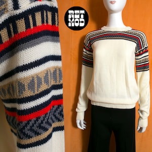 May include: A white knitted sweater with a geometric pattern in shades of brown, red, gray, and black. The sweater has long sleeves and a crew neck.