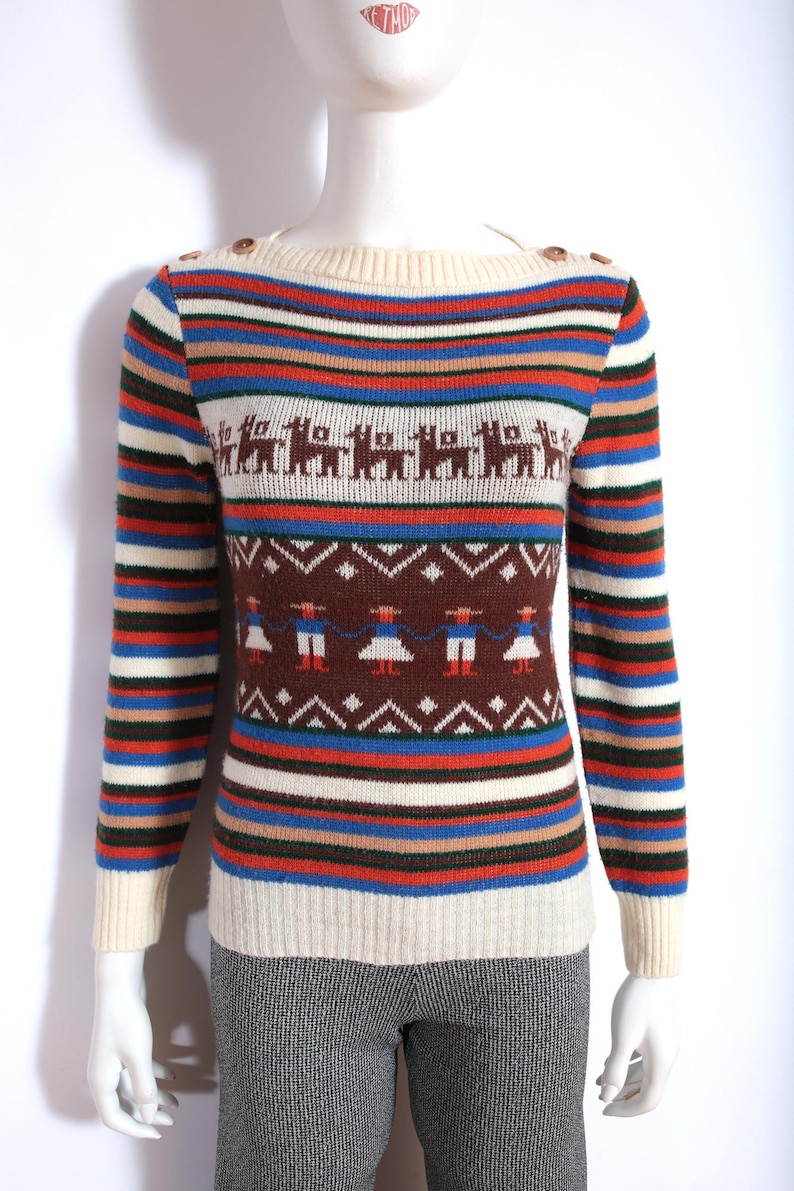 May include: A vintage-style sweater with a cream-colored neckline and cuffs, adorned with brown buttons on the shoulder. The sweater features horizontal stripes in various colors, including blue, red, and brown, and includes patterned sections with llama and figure motifs.
