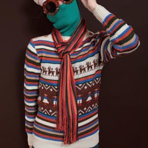 May include: A person wearing a vintage-style outfit. The ensemble includes a cream-colored beret, oversized orange sunglasses, and a green turtleneck. A striped scarf and a sweater with a geometric and animal pattern complete the look. The sweater has horizontal stripes in various colors.
