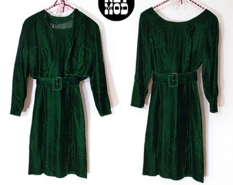 Pode incluir: Um conjunto de vestido e jaqueta combinando em veludo verde com cinto. O vestido e a jaqueta têm mangas compridas e uma silhueta ajustada.
