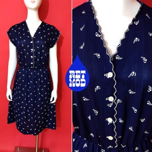 Peut inclure: Robe vintage bleu marine avec une bordure festonnée blanche et un petit motif blanc. La robe présente un col en V, des manches courtes et une fermeture boutonnée sur le devant. La taille est cintrée avec une bande élastique.