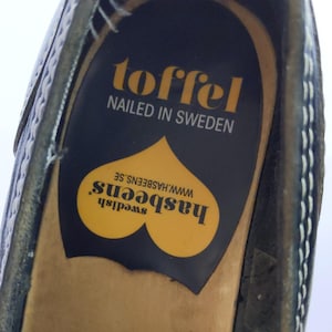 May include: Close-up of a black shoe interior with a yellow and black insole. The insole features the text "toffel, nailed in Sweden" and the brand name "hasbeens" with a heart-shaped design.