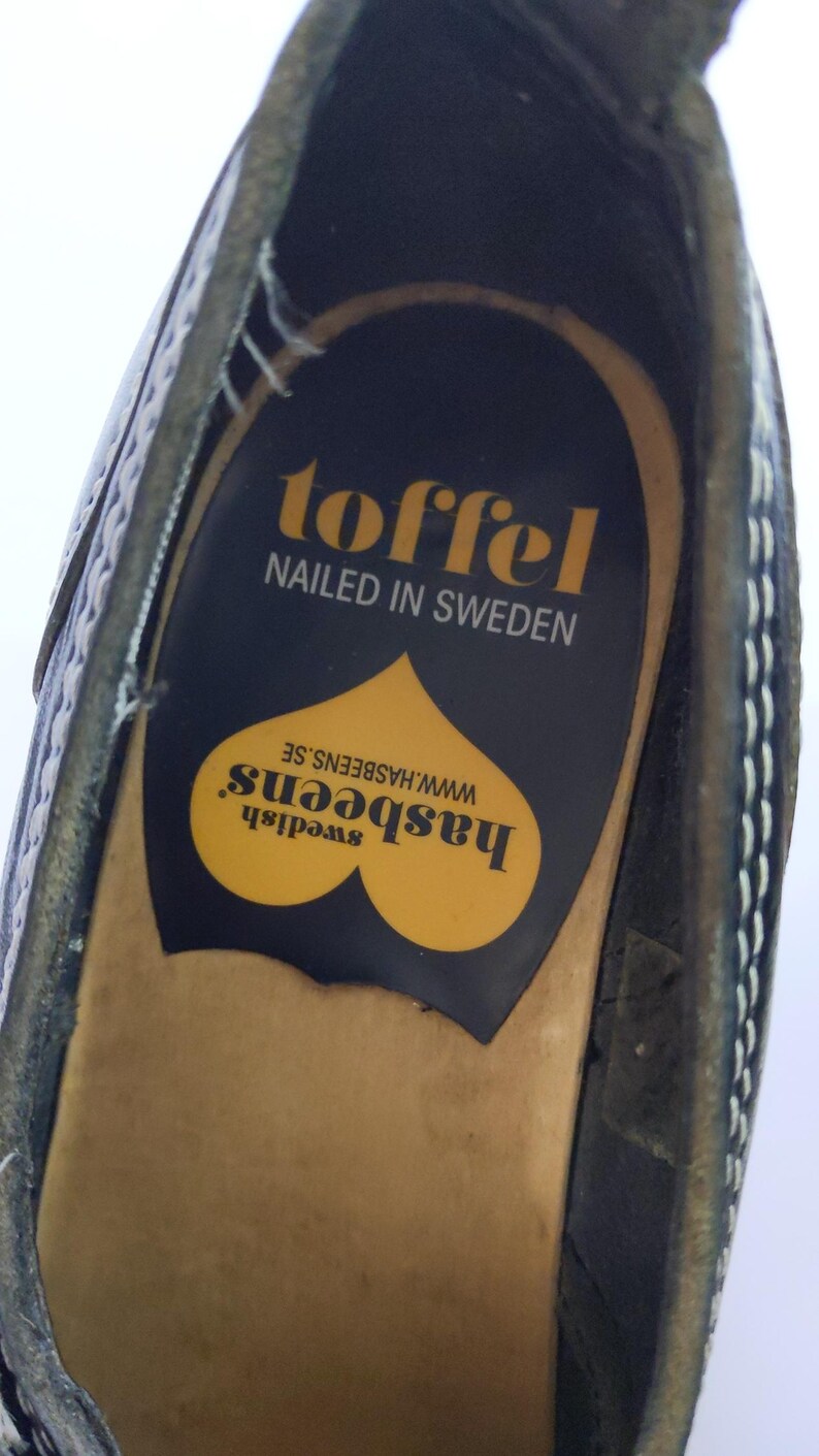 May include: Close-up of a black shoe interior with a yellow and black insole. The insole features the text "toffel, nailed in Sweden" and the brand name "hasbeens" with a heart-shaped design.