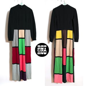 May include: A long black dress with long sleeves and a high neckline. The lower portion of the dress features a geometric color block design in shades of red, pink, green, gray, and beige. The dress is hanging on a white hanger.