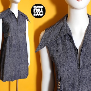 May include: A sleeveless denim dress with a collared neckline and a front zipper. The dress features gold-colored buttons and a belt detail at the waist. The dress is displayed on a mannequin against a yellow background.