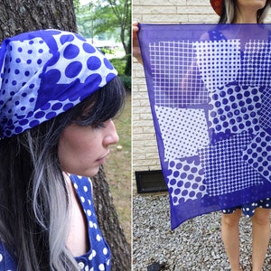 May include: A purple and white patterned bandana with a grid, polka dots, and geometric shapes. The bandana is folded and tied around a person's head.