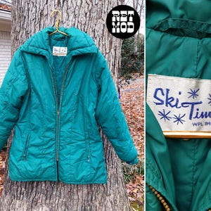 Può includere: Giacca da sci vintage color turchese con zip frontale e ampio colletto. La giacca presenta un'etichetta con la scritta "Ski Time" in blu con dettagli a fiocco di neve. La giacca è appesa a una gruccia dorata.