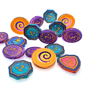 Puede incluir: Una colección de fichas de juego coloridas en varias formas, incluyendo círculos, octágonos y escudos. Las fichas presentan colores morado, naranja y turquesa con números impresos como +1, -2, -3 y +2, junto con gráficos de espirales y estrellas.