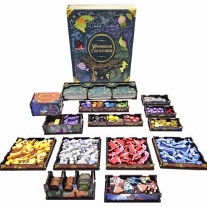 May include: A board game set titled Wondrous Creatures featuring a large rectangular box with dark blue cover art, multiple wooden storage trays, and various game components including yellow, white, red, and blue creature tokens and markers.