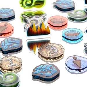 May include: A collection of colorful, translucent glass pendants and charms. Designs include a paw print, a skull, a spiral, and a stylized mountain range. The pendants are in shades of blue, green, orange, and white.