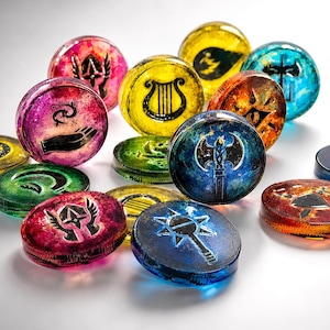 May include: A collection of circular resin tokens in various colors including pink, yellow, blue, green, and orange. Each token features a distinct black graphic symbol, such as a harp, an axe, a hand with stars, a shield, and a mace, embedded within.