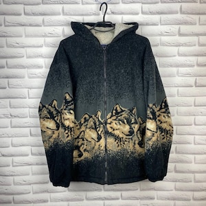 Peut inclure: Veste à capuche noire zippée avec un motif de loup. La veste présente une doublure en sherpa crème dans la capuche et un motif répété de visages de loups dans des tons marron et beige en bas.
