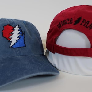 May include: Two baseball caps. One is blue with a red, white, and blue embroidered image of the state of Wisconsin with a lightning bolt. The other is red with black embroidered text that says "Wised Film".