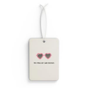 Könnte beinhalten: Weißer Auto-Lufterfrischer mit einem pinkfarbenen Herz-Sonnenbrillen-Motiv und dem Text "Tell your cat I said pspsps"