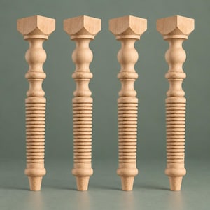 May include: Four unfinished light-colored wooden furniture legs arranged in a row. Each leg features a square top block, a smooth rounded upper section, and a lower portion with a series of horizontal ribbed grooves ending in a tapered base.
