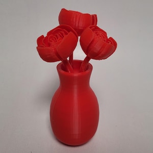 May include: A red vase with three red flowers. The vase is a simple, rounded shape. The flowers are stylized and have a layered, ruffled appearance.