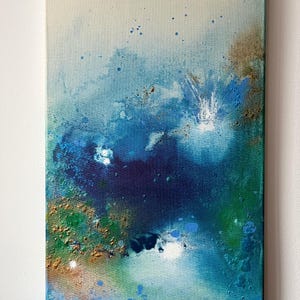 Può includere: Opera d'arte astratta su tela con una miscela di blu, verdi e oro. L'opera presenta una superficie strutturata con spruzzi e colori stratificati, creando una composizione dinamica. Il dipinto è montato su una tela rettangolare.