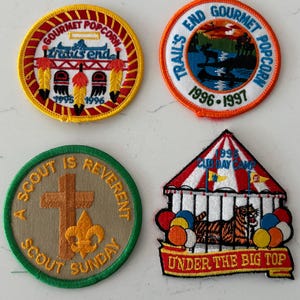 Puede incluir: Cuatro parches bordados con varios diseños. Dos parches circulares presentan el texto "Gourmet Popcorn" y "Trail's End Gourmet Popcorn". Otro parche dice "A Scout is Reverent Scout Sunday". El parche final es una carpa de circo con un tigre y el texto "Under the Big Top."