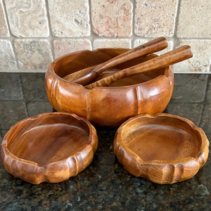 Pode incluir: Um conjunto de saladeira de madeira com duas tigelas menores e duas colheres de servir de madeira. As tigelas e colheres são feitas de madeira castanha clara e têm um acabamento natural. As tigelas têm uma borda ondulada.