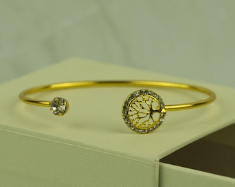 May include: A gold bangle bracelet with a circular charm featuring a tree design with clear rhinestones. The bracelet is displayed in a white box.