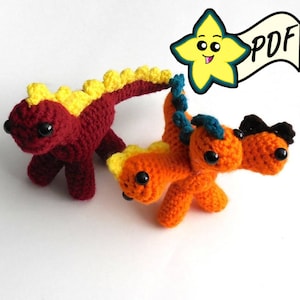 Peut inclure: Deux jouets en crochet en forme de dinosaure. L'un est rouge avec des accents jaunes et l'autre est orange avec des accents bleus et noirs. Le dinosaure orange a trois têtes.