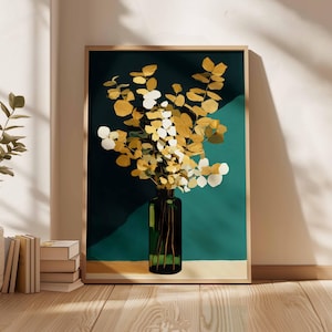 May include: A framed art print featuring a vase of golden and white leaves against a teal background. The vase is dark green, and the frame is a light wood color. The artwork is displayed on a wall with natural light.
