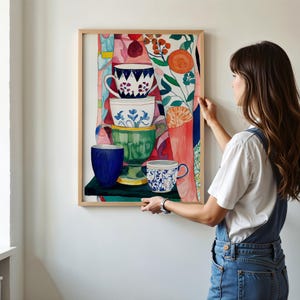 Kitchen-inspired still life artwork showing stacked ceramic teacups painted in watercolor. Floral motifs, textured brushstrokes, and a colorful background create a lively composition. Botanical elements and patterned shapes enhance the sense of warmth and domestic comfort associated with tea time and daily routines.