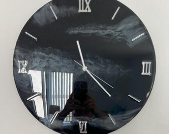 May include: Black and white clock with Roman numeral markings. The clock face has a white marbled design on a black background.