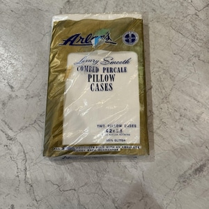 May include: A package of two white pillowcases, labeled "Luxury Smooth Combed Percale." The packaging is gold and white, with the brand name "Arlons" in a stylized font. The pillowcases measure 42 x 38 inches and are made of 100% cotton.