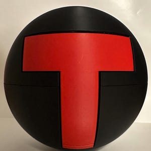 May include: A black sphere with a large red 'T' shape in the center. The 'T' is a solid, bold design, contrasting sharply against the black background. The sphere appears to be made of a matte material.