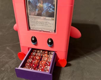 May include: A pink 3D-printed card holder with a drawer filled with red dice. The holder features a card with the text "Glada, Font of Hope" and cartoon-like eyes and arms. A fun and functional accessory for card game enthusiasts.