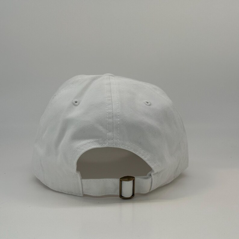May include: A white baseball cap with a curved brim. The back of the cap features an adjustable strap with a metal buckle. The cap is made of a soft, cotton-like material.