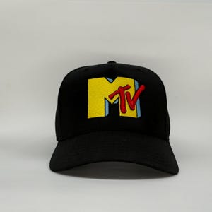 Peut inclure: Casquette de baseball noire avec le logo MTV brodé sur le devant. Le logo est jaune, rouge et bleu. La casquette a une visière incurvée et une coupe structurée.